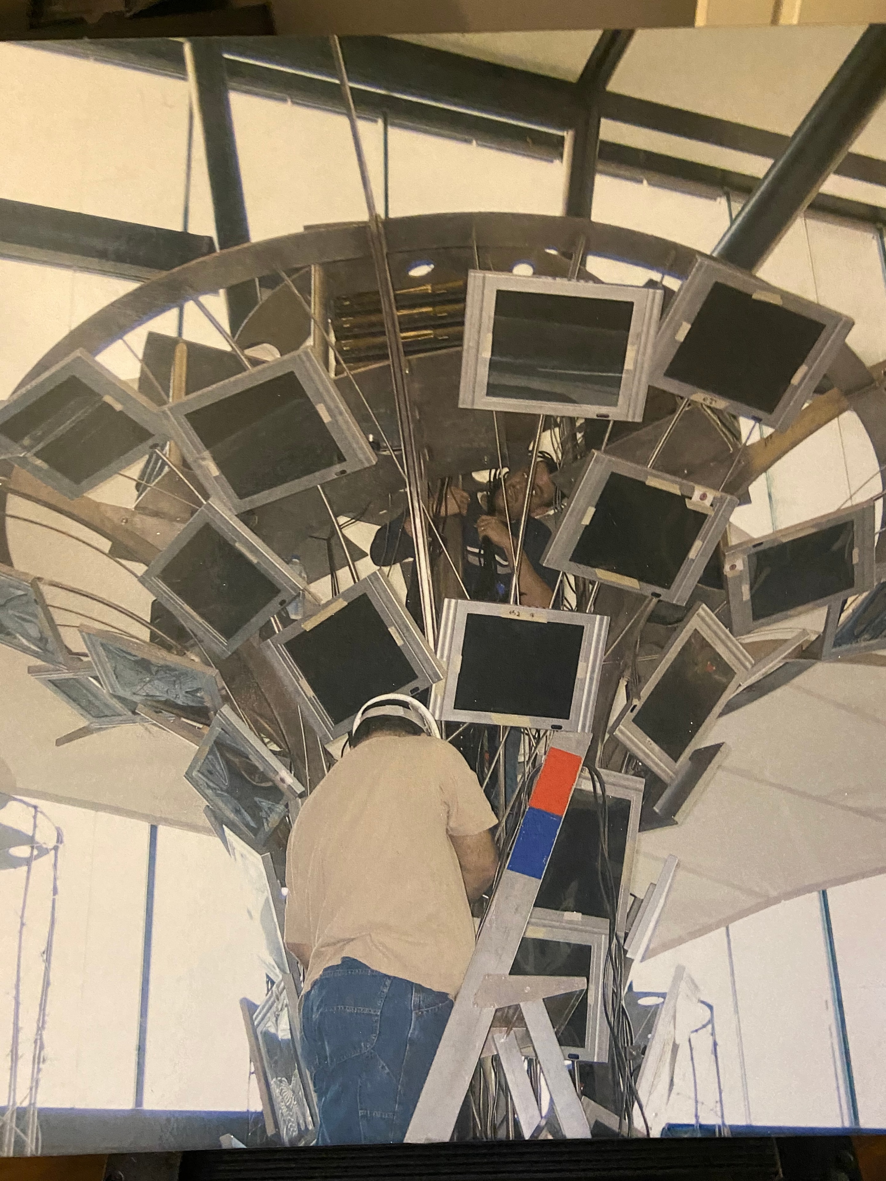 Person climbing spherical structure with old monitors — legacy AV removal